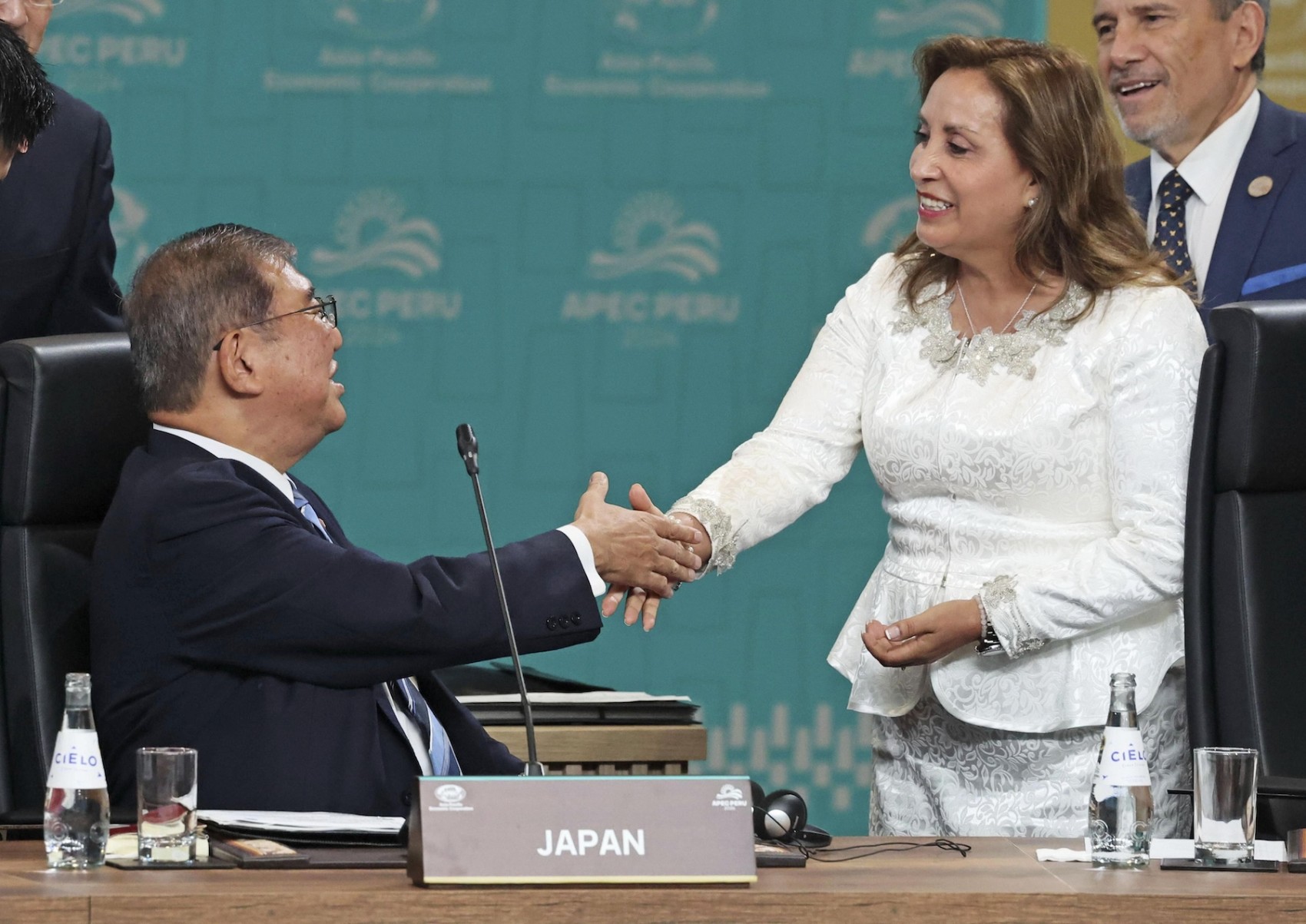 Japanese Prime Minister Shigeru Ishiba shakes hands while seated with Peruvian President Dina Boluarte